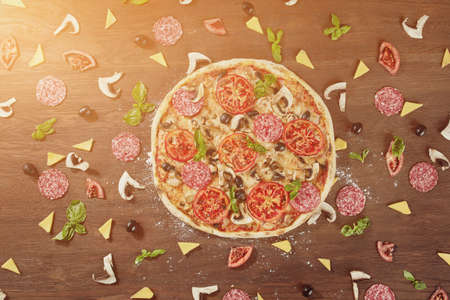 Pizza with tomatoes, mozzarella cheese, black olives and basil. Delicious italian pizza on wooden pizza board.の写真素材