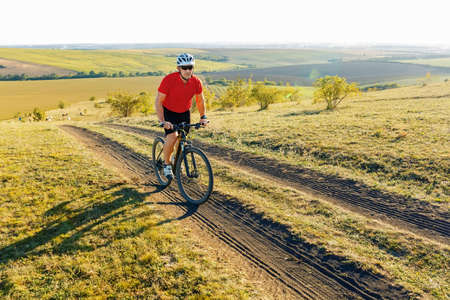 Bike adventure travel photo. Bike tourist rides on the country road. Sunset on background.の写真素材