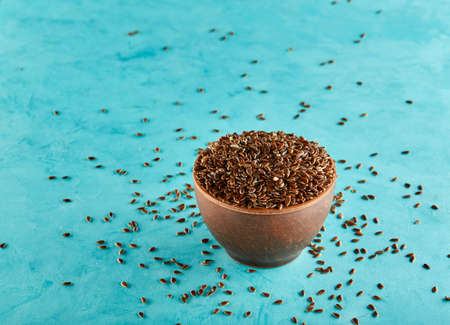 Flax seeds in a clay bowl isolated on blue background, close-up