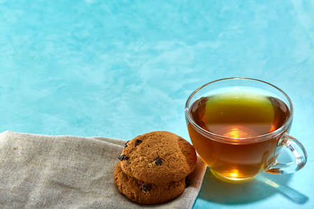 Glass cup of tea and oatmeal chocolate cookies close-up on blue background.