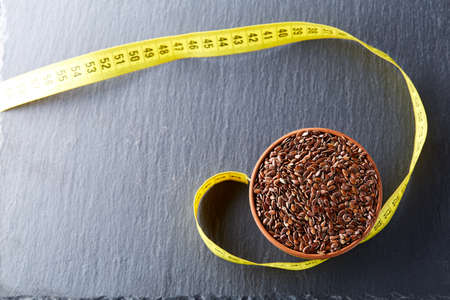 Many flax seeds are scattered in the background, and poured into a clay plate, space for textの写真素材
