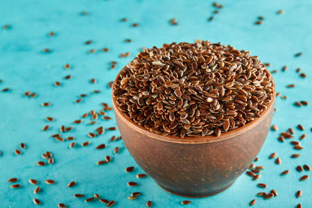 Flax seeds in a clay bowl isolated on blue background, close-up, selective focus, vertical.の写真素材