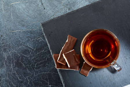 glass cup of black tea with chocolate pieces on a dark greyish marble background. Top viewの写真素材