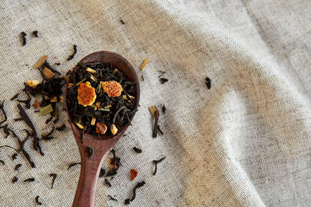 Closeup of a dark brown longhandled wooden spoon filled with scattered tea leaves and tiny pieces of dried citrus on light grey textured tablecloth. Shallow depth of field, selective focus, front focus.の写真素材