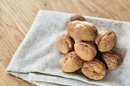 A stack of hard shells of walnuts piled together on light grey fabric cotton napkin and isolated on rustic wooden background, copy space, shallow depth of field, selective focus, front focus, macro. Nutritious food. Healthy lifestyle concept.の写真素材