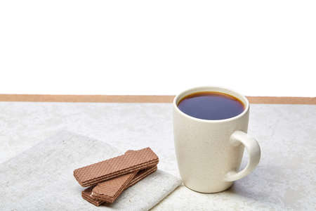 White ceramic porcelain coffeecup with stack of waffles on white cotton napkin on light concrete background, top view. Pleasure coffetime. Tasty aromatic energy drink.の写真素材