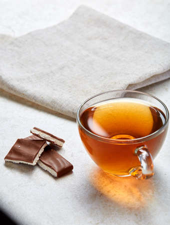 Top view close up picture of earl grey or black tea in transparent glass cup with chocolate pieces next to a cotton napkin on white background, selective focus. Delicious dessert and refreshing teatime. Breakfast background.の写真素材