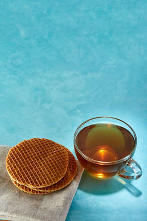 Glass cup of tea and oatmeal chocolate cookies on homespun cotton napkin close-up on blue...