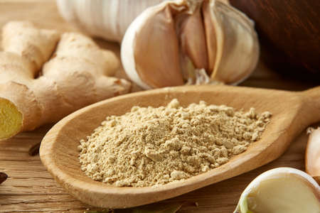 Composition of powder spices on spoon, yellow, red and black peppercorn in ceramic bowl and garlic, ginger, cinnamon, clove and bay leaf on rustic wooden table background, close-up, top view, selective focus, shallow depth of field.の写真素材