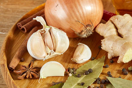 Conceptual composition of different spices on a wooden tray on a rustic table: onion, garlic,...