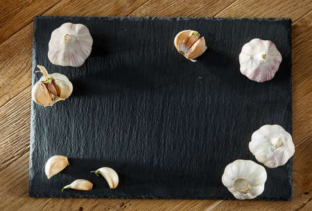 Garlic composition on black flat piece of board on rustic rough wooden background copy space for your text. Close-up, macro. Aromatic and gourmet combination of garlic bulbs. Heart diseases prevention. Healthy lifestyle concept.の写真素材