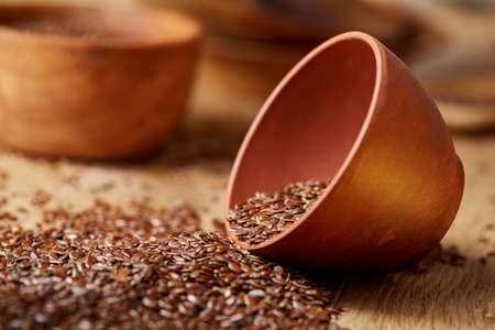 An overturned ceramic clay bowl with linseeds on a brown rustic wooden background seen from the opening, close-up, shallow depth of field, selective focus, front focus. Healthy lifestyle concept.の写真素材