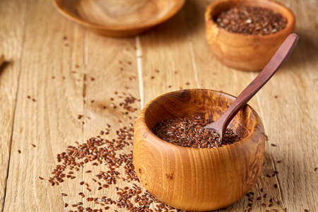 Top view close-up picture of flax seeds in wooden bowl and spoon isolated on brown rustic wooden background, shallow depth of field, selective focus, front focus. Nutritious and deitary ingredient. Healthy lifestyle concept.の写真素材
