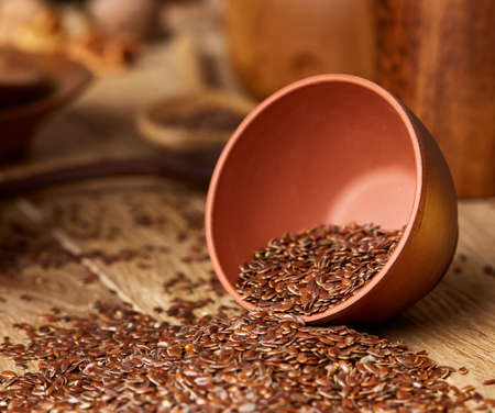 An overturned ceramic clay bowl with linseeds on a brown rustic wooden background seen from the opening, close-up, shallow depth of field, selective focus, front focus. Healthy lifestyle concept.の写真素材