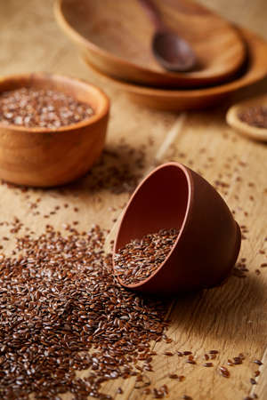 An overturned ceramic clay bowl with linseeds on a brown rustic wooden background seen from the opening, close-up, shallow depth of field, selective focus, front focus. Healthy lifestyle concept.の写真素材