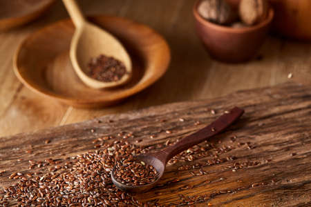 Top view, close-up picture of wooden spoon full of flax seeds over some seeds composed on rustic brown wooden background, shallow depth of field, selective focus, front focus. Organic ingredient for healthy lifestyleの写真素材