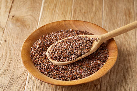 Top view, close-up picture of wooden spoon full of flax seeds over some seeds in the plate composed on rustic brown wooden background, shallow depth of field. Organic ingredient for healthy lifestyleの写真素材