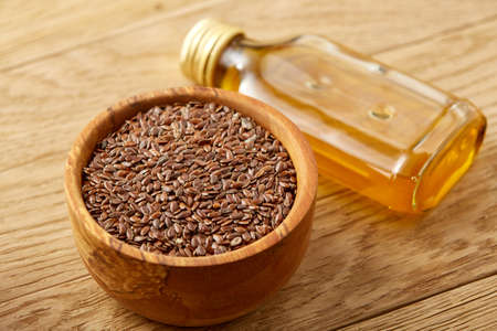 Brown flax seeds in wooden plate and flaxseed oil in glass bottle on brown rustic wooden background, top view, close-up, selective focus. Flax oil is rich in omega-3 fatty acid. Healthy lifestyle concept.の写真素材