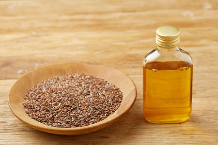 Brown flax seeds in wooden plate and flaxseed oil in glass bottle on brown rustic wooden background, top view, close-up, selective focus. Flax oil is rich in omega-3 fatty acid. Healthy lifestyle concept.の写真素材