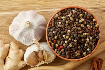 Composition of powder spices on spoon, yellow, red and black peppercorn in ceramic bowl and garlic, ginger, cinnamon, clove and bay leaf on rustic wooden table background, close-up, top view, selective focus, shallow depth of field.の写真素材
