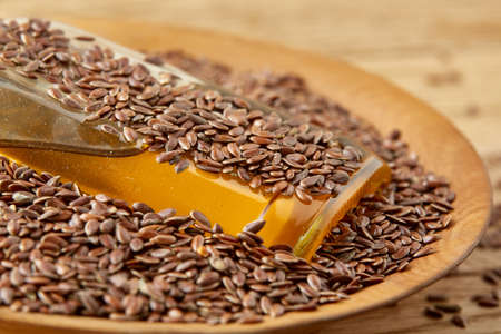 Linseed oil in a glass bottle in the clay ceramic plate full of raw flax seeds on a brown rustic wooden table background, top view, close-up, shallow depth of field, selective focus, front focus. Healthy lifestyle concept.の写真素材