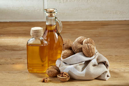 Composition of aromatic oil in a glass jar and bottle with unpeeled peanuts in bowl on wooden table...