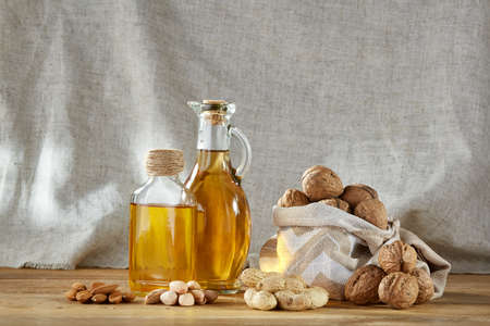 Conceptual composition of transparent glass oil jars with different kinds of nuts such as walnut, peanut, pistachio and almond on rustic wooden table, close-up. Healthy eating, therapeutic and bodycare concept.の写真素材