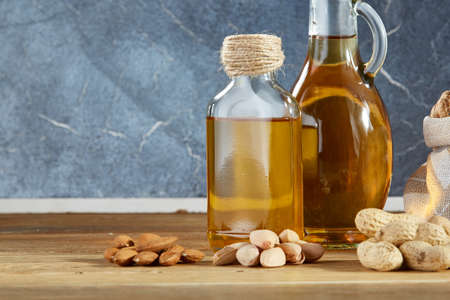 Conceptual composition of transparent glass oil jars with different kinds of nuts such as walnut, peanut, pistachio and almond on rustic wooden table, close-up. Healthy eating, therapeutic and bodycare concept.の写真素材