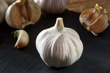 Garlic on flat black piece of board. Close-up, shallow depth of field, selective focus, front focus, macro. Aromatic and gourmet combination of garlic bulbs. Heart diseases prevention. Healthy lifestyle concept.の写真素材