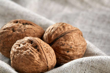 A stack of hard shells of walnuts piled together on light grey fabric cotton tablecloth, copy space, shallow depth of field, selective focus, front focus, macro. Nutritious food. Healthy lifestyle concept.の写真素材