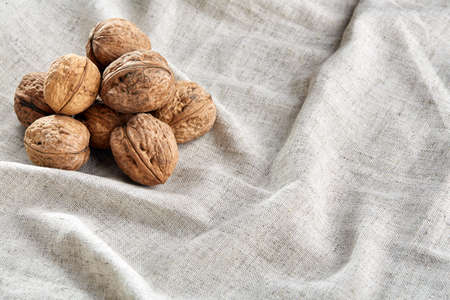 A stack of hard shells of walnuts piled together on light grey fabric cotton tablecloth, copy space, shallow depth of field, selective focus, front focus, macro. Nutritious food. Healthy lifestyle concept.の写真素材