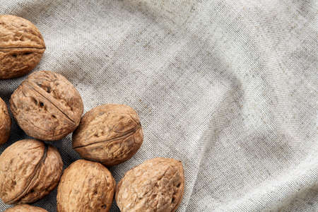 A stack of hard shells of walnuts piled together on light grey fabric cotton tablecloth, copy space, shallow depth of field, selective focus, front focus, macro. Nutritious food. Healthy lifestyle concept.の写真素材