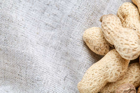 Top view close-up picture of heap of peanuts on light grey fabric cotton tablecloth or napkin, some copy space, shallow depth of field, selective focus, front focus. Tasty and diet snack. Healthy lifestyle concept.の写真素材