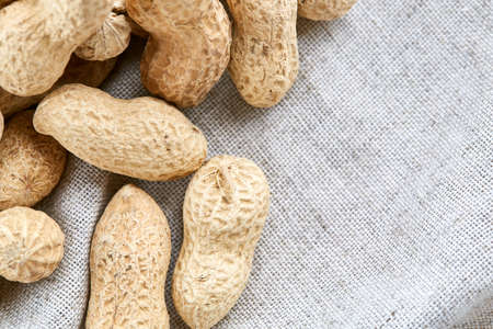 Top view close-up picture of heap of peanuts on light grey fabric cotton tablecloth or napkin, some copy space, shallow depth of field, selective focus, front focus. Tasty and diet snack. Healthy lifestyle concept.の写真素材