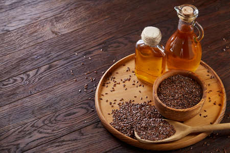 Flax seeds in bowl and flaxseed oil in glass bottle on wooden background, top view, close-up, selective focusの写真素材