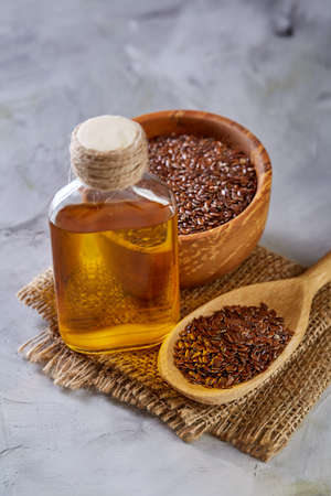 Flax seeds in bowl and flaxseed oil in glass bottle on light textured background, top view, close-up, selective focusの写真素材