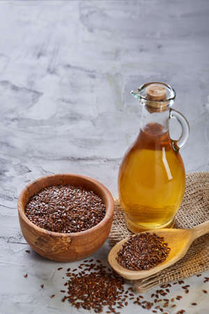 Flax seeds in bowl and flaxseed oil in glass bottle on light textured background, top view, close-up, selective focusの写真素材