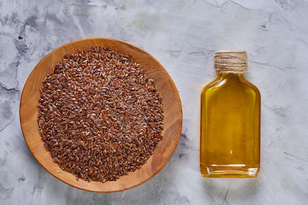 Flax seeds in bowl and flaxseed oil in glass bottle on light textured background, top view, close-up, selective focusの写真素材