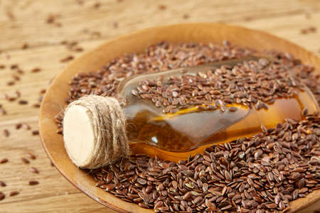 Top view closeup picture flax seeds and linseed oil in a glass bottle on a wooden background, shallow depth of field.の写真素材