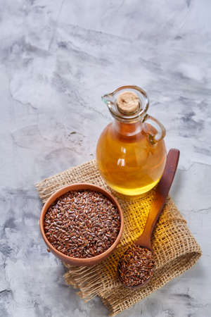 Flax seeds in bowl and flaxseed oil in glass bottle on light textured background, top view, close-up, selective focusの写真素材