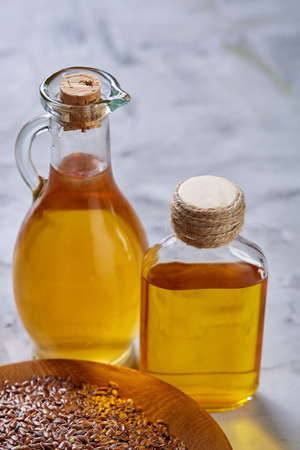 Flax seeds in bowl and flaxseed oil in glass bottle on light textured background, top view, close-up, selective focusの写真素材