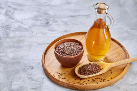 Flax seeds in bowl and flaxseed oil in glass bottle on light textured background, top view, close-up, selective focusの写真素材
