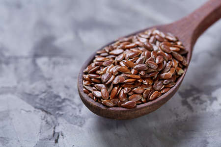 Wooden spoon with flax seeds on light textured background, top view, close-up, shallow depth of field, selective focusの写真素材