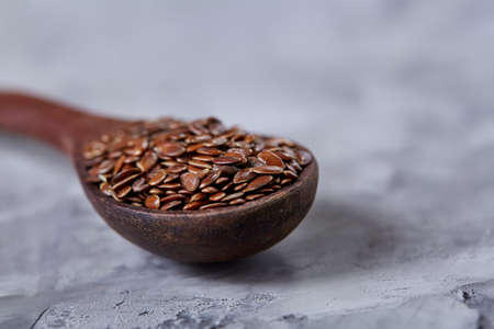 Wooden spoon with flax seeds on light textured background, top view, close-up, shallow depth of field, selective focusの写真素材
