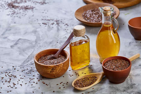 Flax seeds in bowl and flaxseed oil in glass bottle on light textured background, top view, close-up, selective focusの写真素材