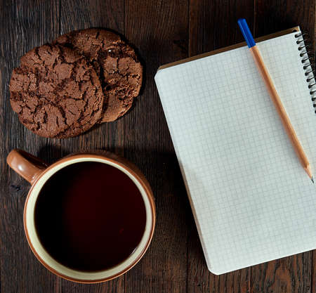 Cup of tea with cookies, workbook and a pencil on a wooden background, top viewの写真素材