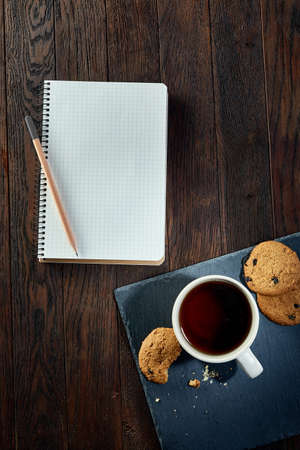 Cup of tea with cookies, workbook and a pencil on a wooden background, top viewの写真素材