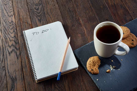 Cup of tea with cookies, workbook and a pencil on a wooden background, top viewの写真素材