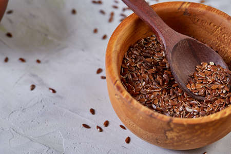 Flax seeds in wooden bowl and wooden spoon on light textured background, top view, shallow depth of field, selective focus, front focus. Nutritious organic condiment. Healthy lifestyle concept.の写真素材