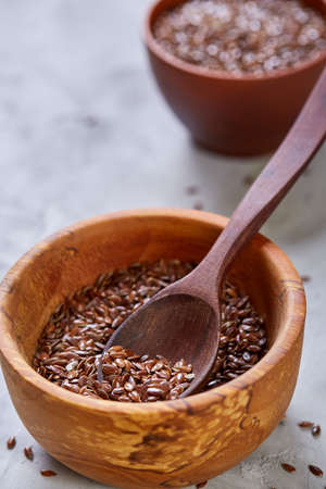 Flax seeds in wooden bowl and wooden spoon on light textured background, top view, shallow depth of field, selective focus, front focus, vertical. Nutritious organic condiment. Healthy lifestyle concept.の写真素材